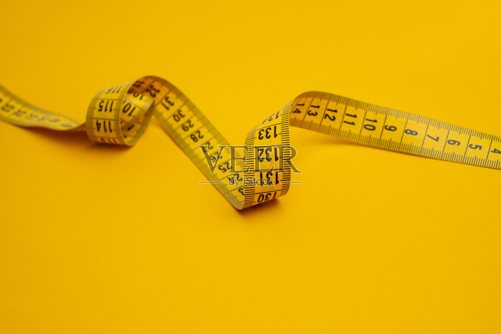 黄色的卷尺在黄色背景上。用于测量长度和体积的工具。用于服装行业或人体体积测量的卷尺。照片摄影图片