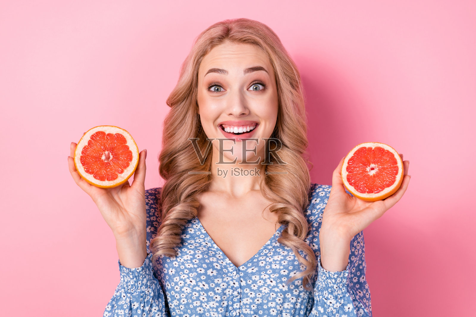 一位迷人的积极人士微笑着，双手各持一半的葡萄柚，背景为粉色。照片摄影图片
