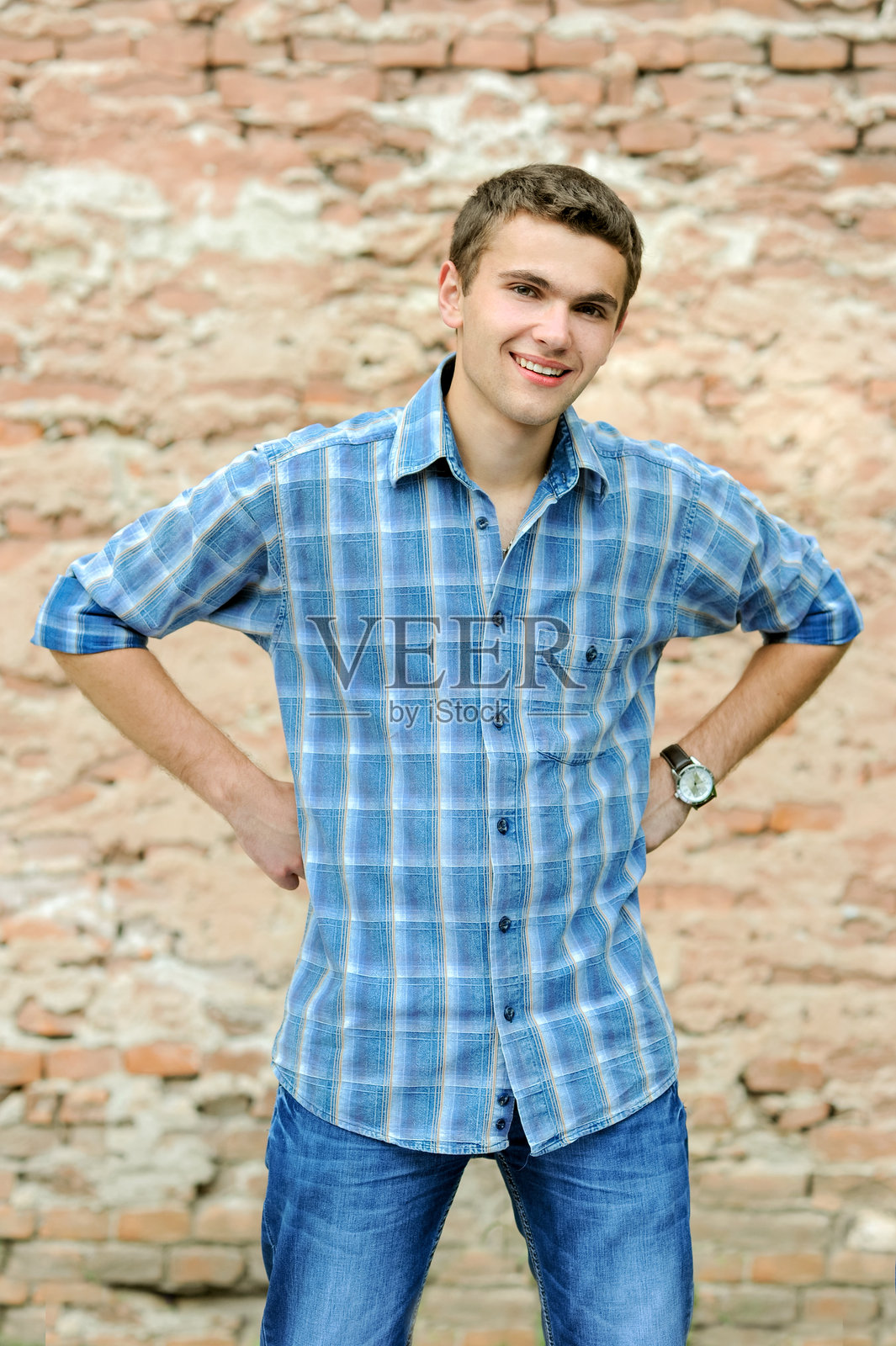 穿着格子衬衫的年轻男子双手垂在身侧，微笑着展现出自信和快乐。照片摄影图片