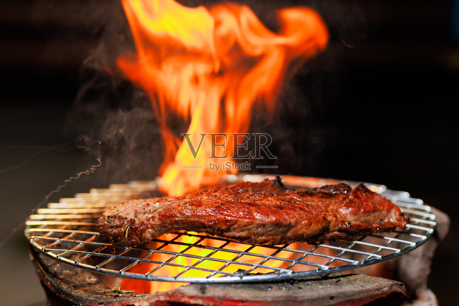 一块厚实多汁的牛排在热烤架上滋滋作响，火焰在其下升腾，捕捉着明火烹饪的强烈热量和风味。照片摄影图片