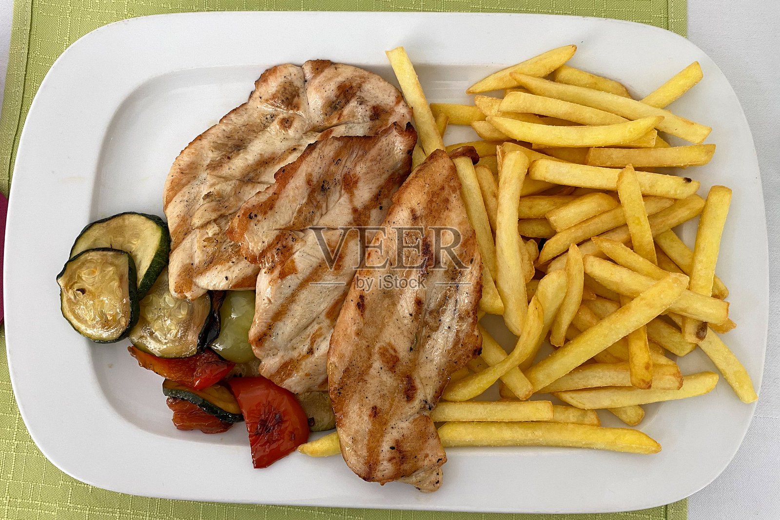 白盘上盛着烤鸡胸肉，配有脆薯条和混合蔬菜照片摄影图片