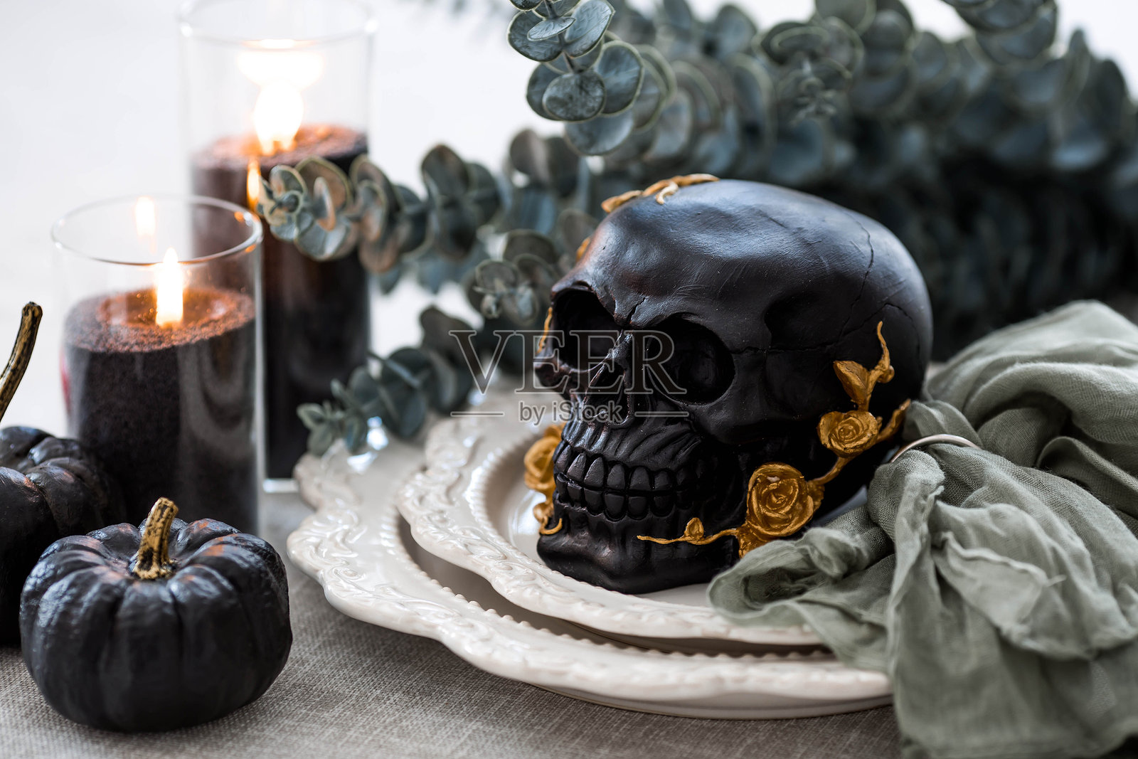 一个神秘的黑色骷髅，上面装饰着金色玫瑰和南瓜，摆放在盘子上，适合万圣节或亡灵节派对。照片摄影图片