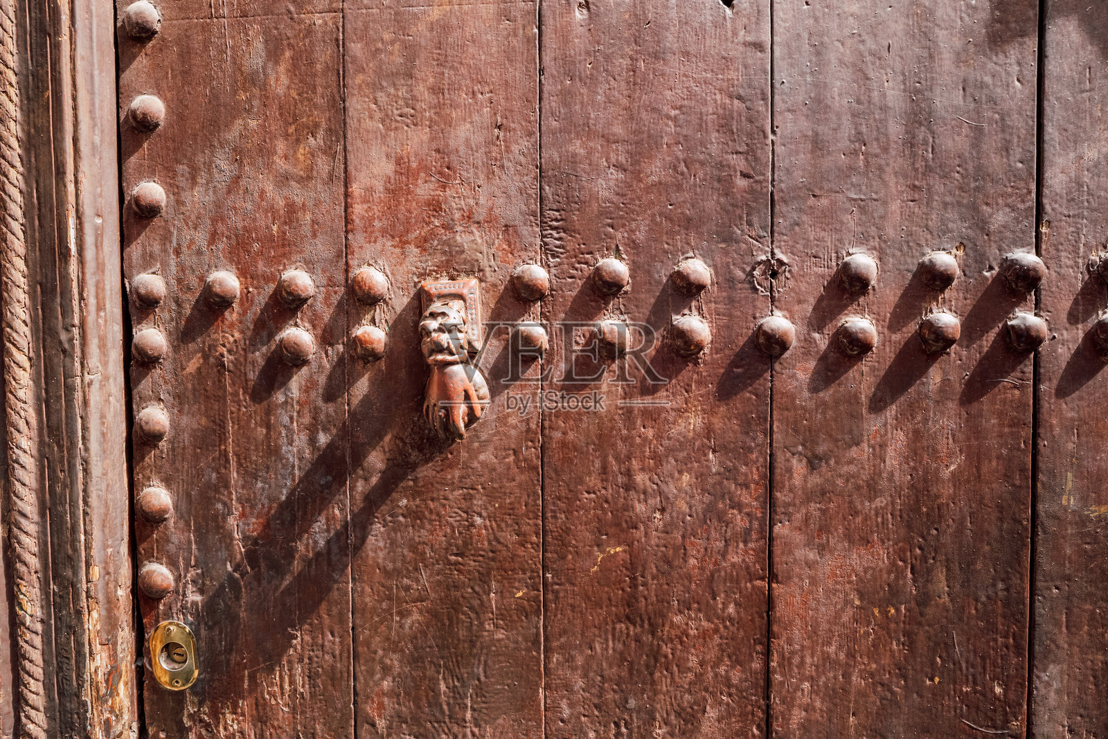 特写一扇风化的木门，门上有装饰性的金属门环和一排排铆钉，展示了传统的摩洛哥工艺。照片摄影图片