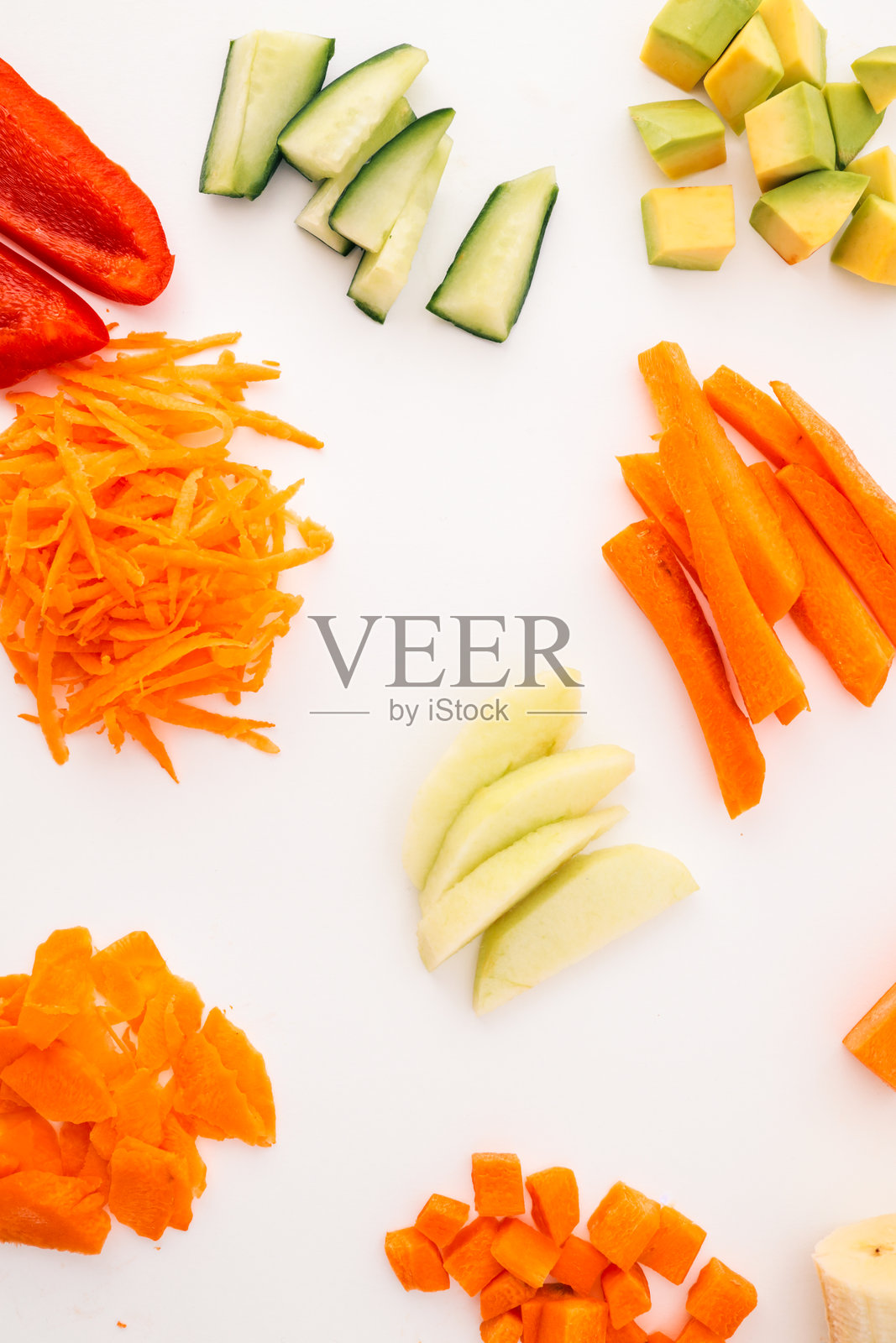 新鲜切好的蔬菜和水果的组合，摆放在白色背景上。包括胡萝卜、黄瓜、鳄梨、苹果、香蕉、甜椒和番茄，采用不同的切割方式，适用于烹饪概念。照片摄影图片