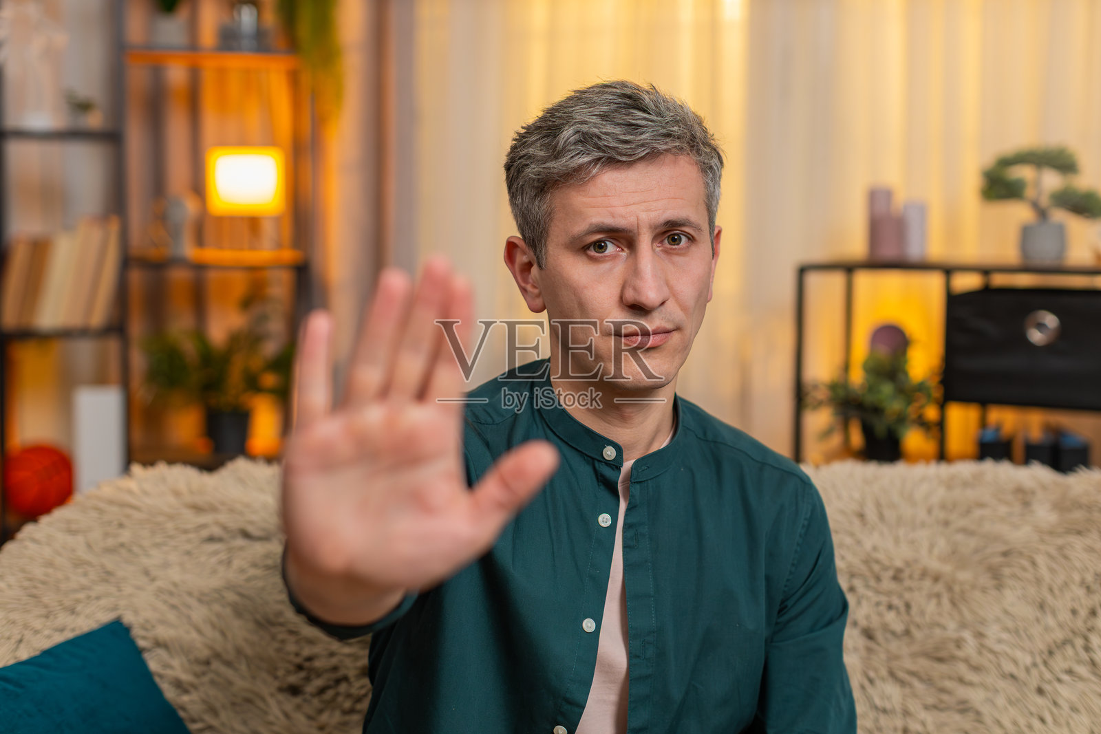 年轻男子用举起的手做出停止的手势，面带严肃表情，表达情感界限或拒绝。照片摄影图片