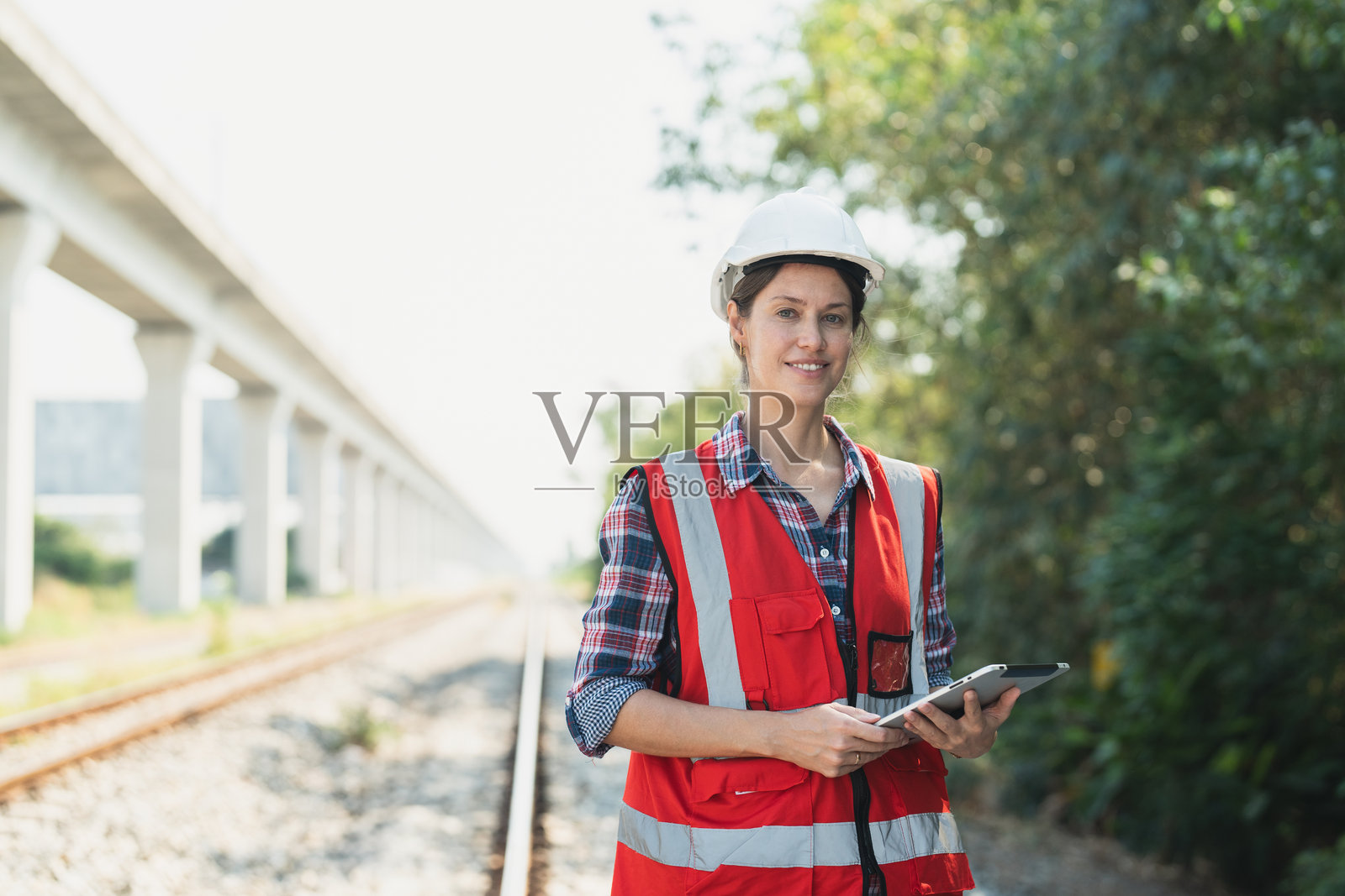 铁路女工程师穿着安全背心和头盔，手持平板电脑，进行铁路轨道的维护和工作。照片摄影图片