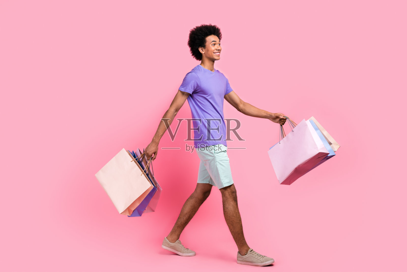 全身照，积极向上的男士穿着时尚的T恤和白色裤子，手持购物服装，背景为空白的粉色。照片摄影图片