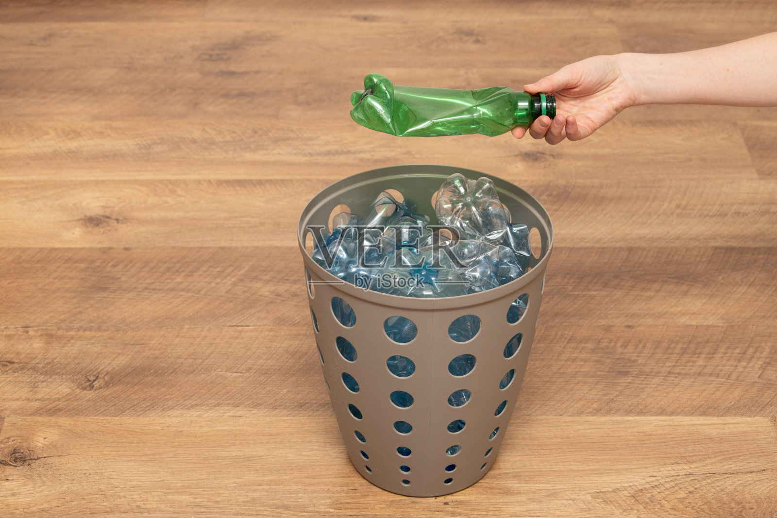 一个人正在积极分类可回收材料，将一个绿色塑料瓶放入装满蓝色瓶子的容器中。这项活动促进了废物管理和回收倡议。照片摄影图片