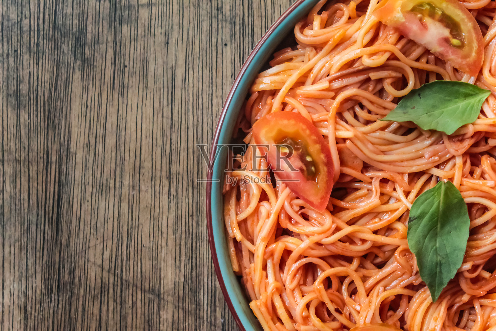 意大利肉酱面特写，盘子上配有切片番茄和罗勒叶，放在木桌上，周围留有负空间。照片摄影图片