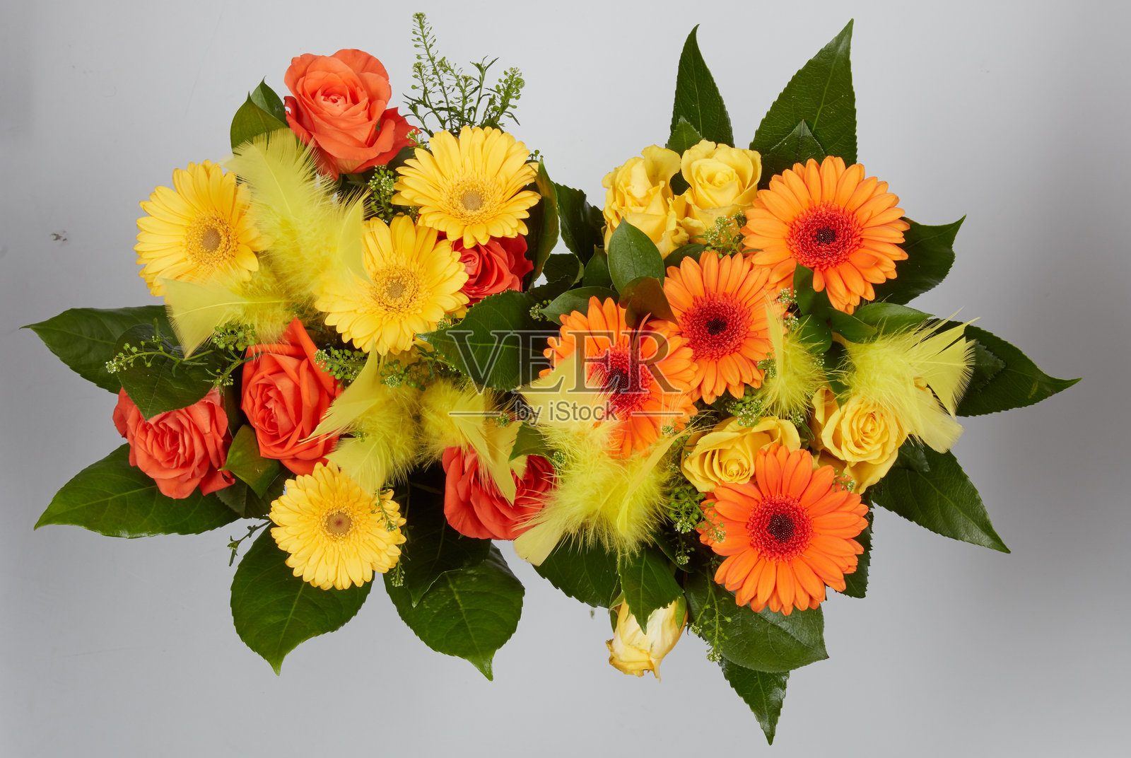 一束黄色和橙色花朵，搭配黄色羽毛，背景为自然风景，带有抠图路径。照片摄影图片