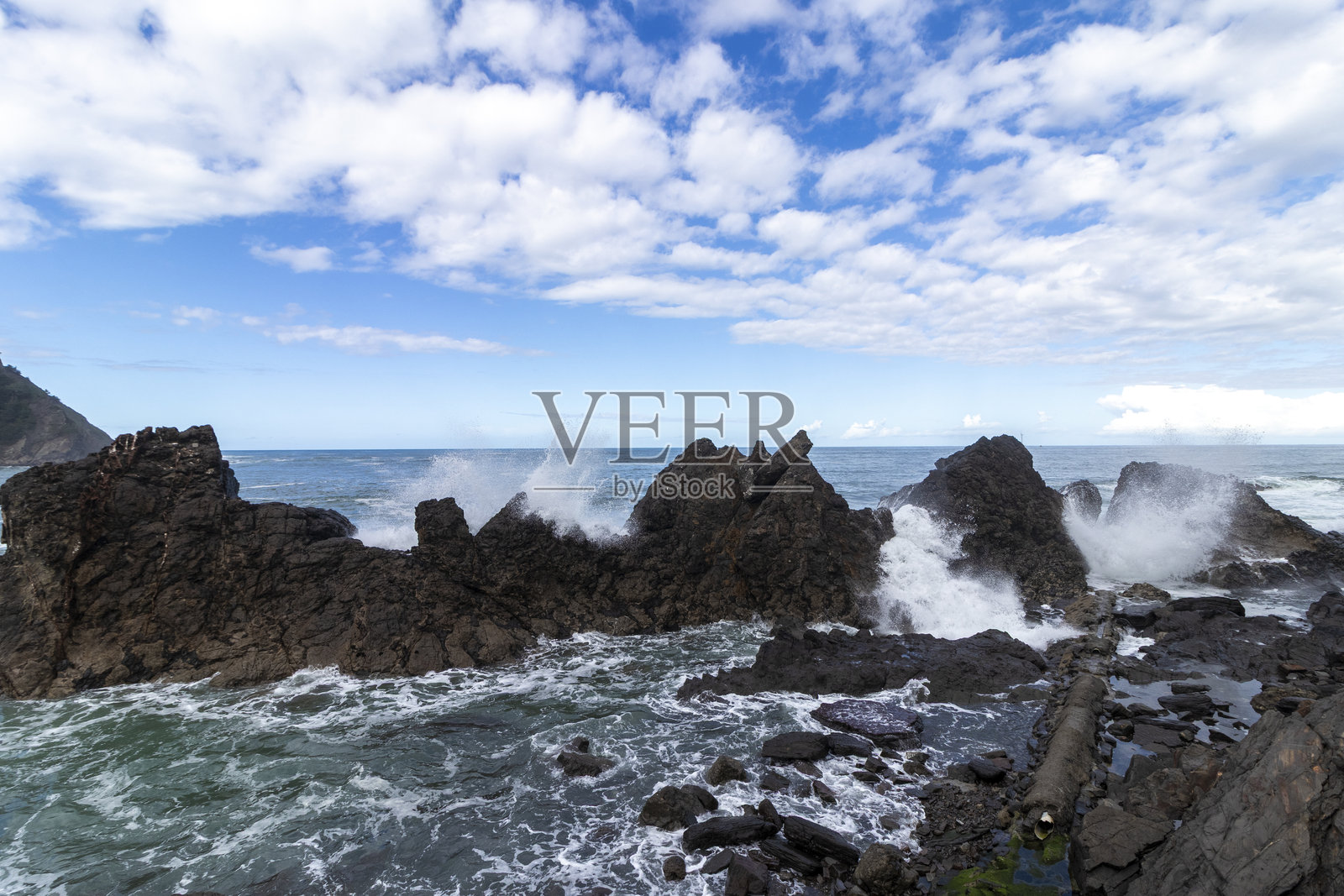 阳光明媚的日子里，海浪拍打在岩石上照片摄影图片