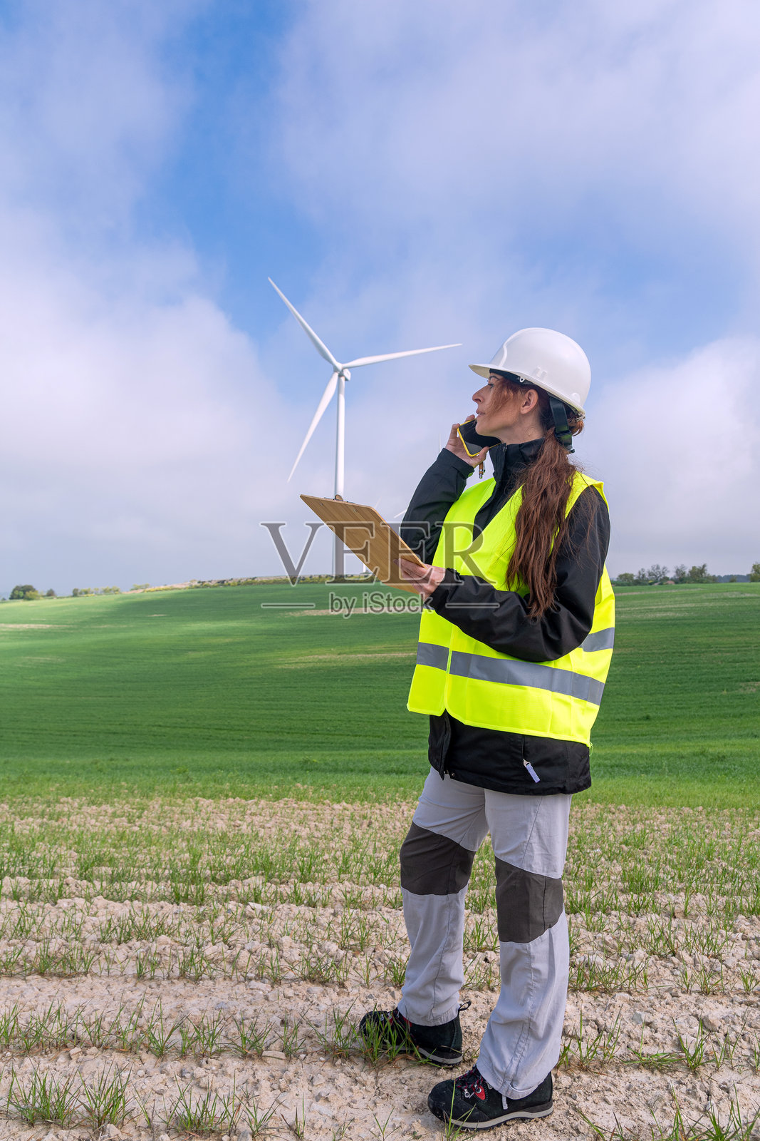 女性工程师在绿色田野中使用手机，靠近风力涡轮机照片摄影图片