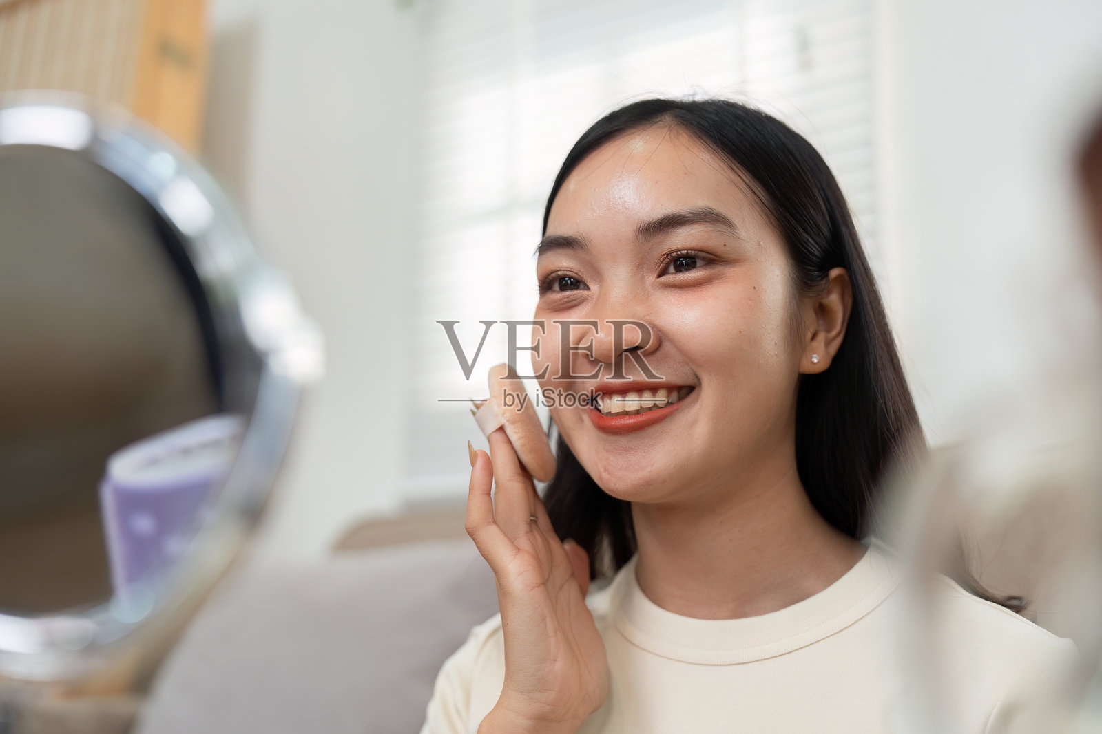 护肤与快乐。一位女性在镜子前微笑着涂抹护肤产品。照片摄影图片