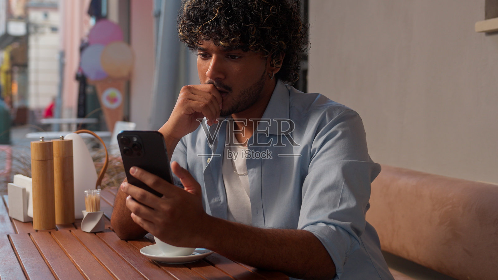 印度男性阿拉伯男学生游客在城市咖啡馆喝咖啡，沉思的商人选择旅行票务服务应用，在线下单支付，手机购物，户外活动。照片摄影图片