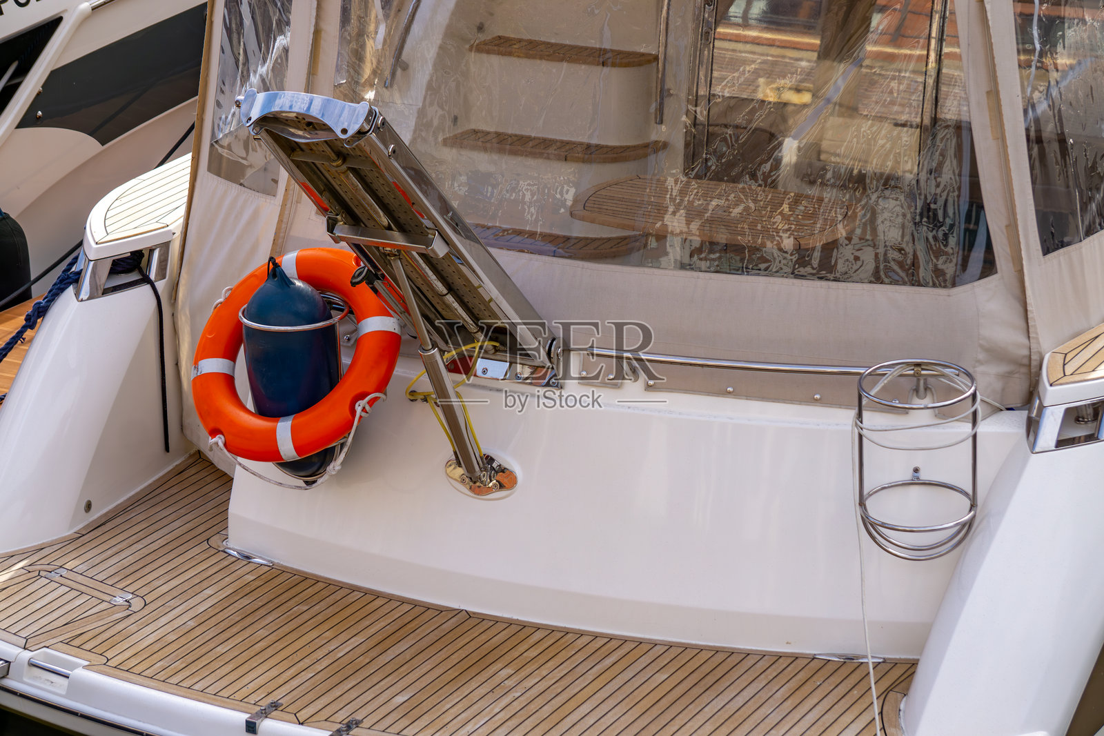 现代摩托游艇的船尾，配有可见的登船梯、橙色救生圈和蓝色护舷。甲板采用浅色柚木装饰，展示了停靠在码头的船只上的标准安全设备。非常适合展示航海主题。照片摄影图片