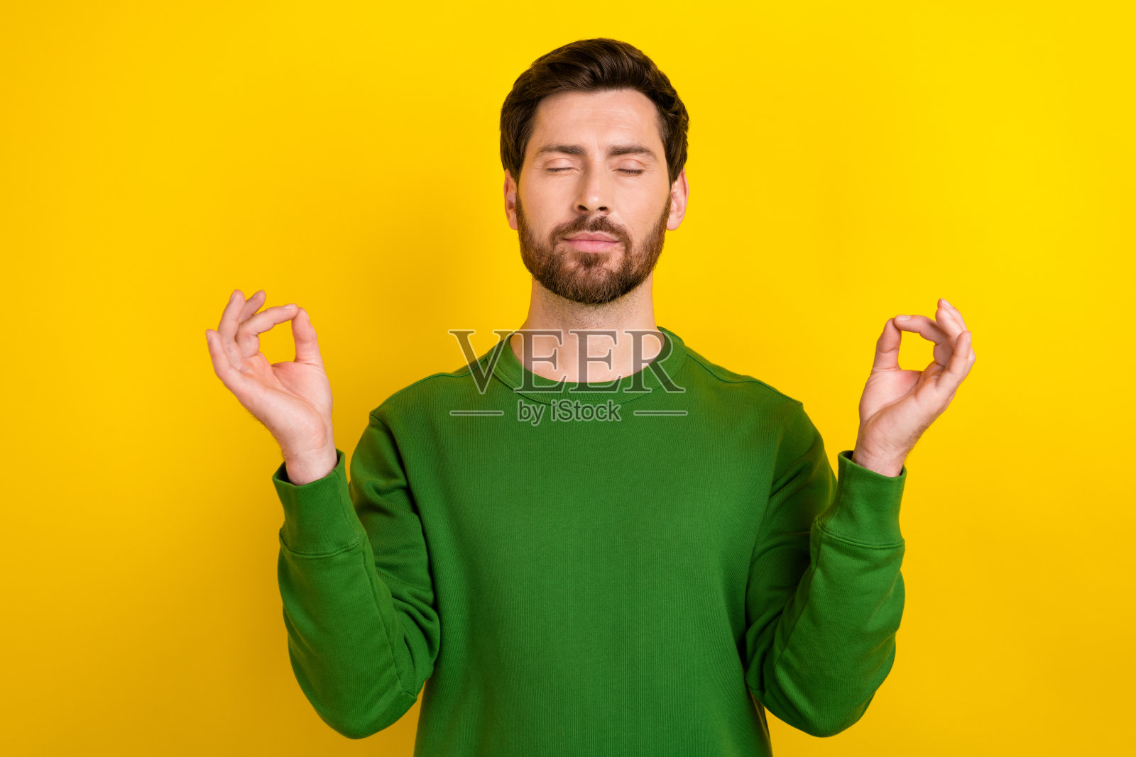 快乐平静的男人穿着绿色毛衣，冥想享受瑜伽练习，梦幻般的“哦姆”放松休息，背景为黄色。照片摄影图片