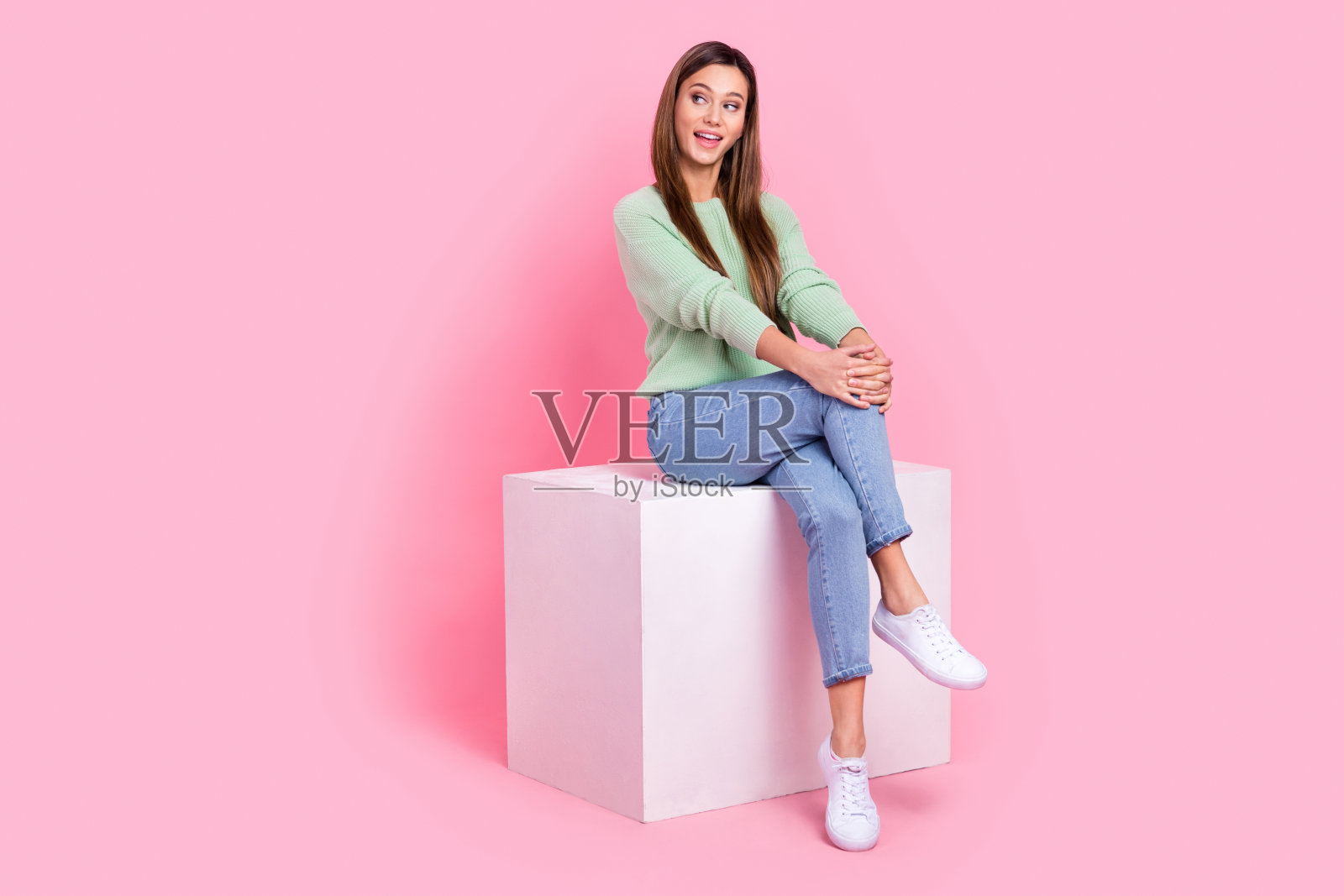全身坐在讲台上的迷人年轻女性，棕色头发，享受她的新装扮，背景为粉色。照片摄影图片