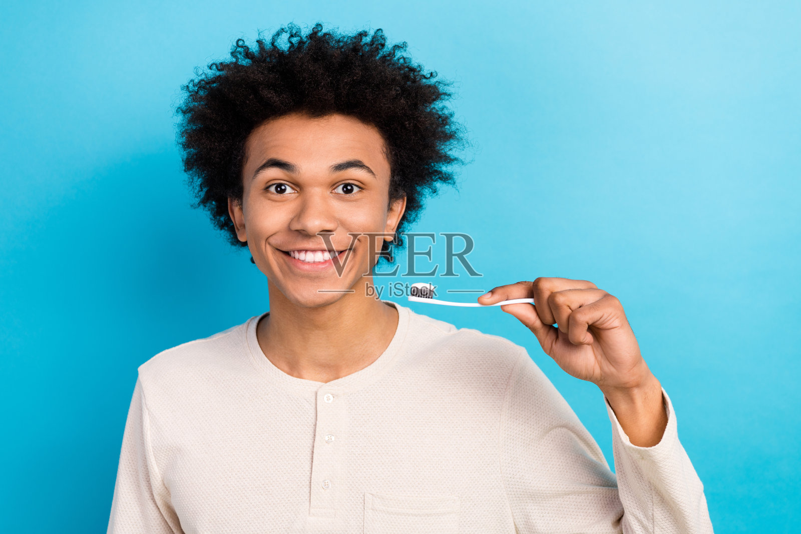 吸引人的年轻男子穿着白色睡衣，手持牙刷，展现健康的牙齿，背景为蓝色。照片摄影图片