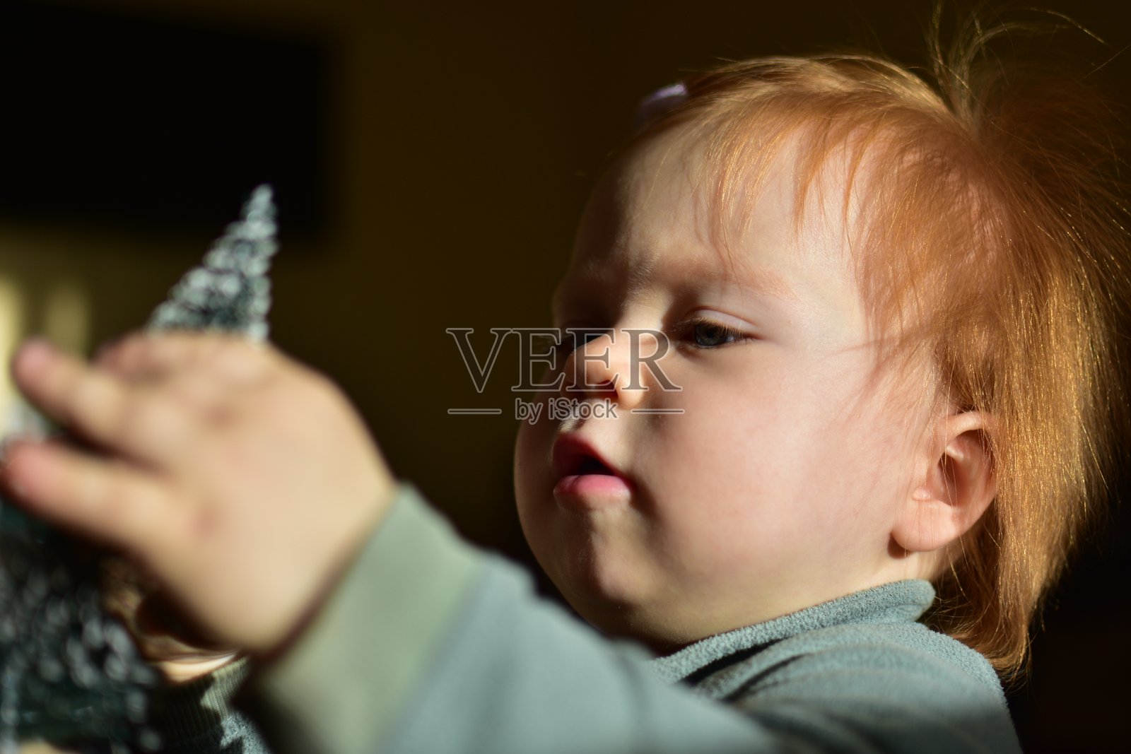 小女孩用红色头发好奇地触摸圣诞树装饰品。照片摄影图片