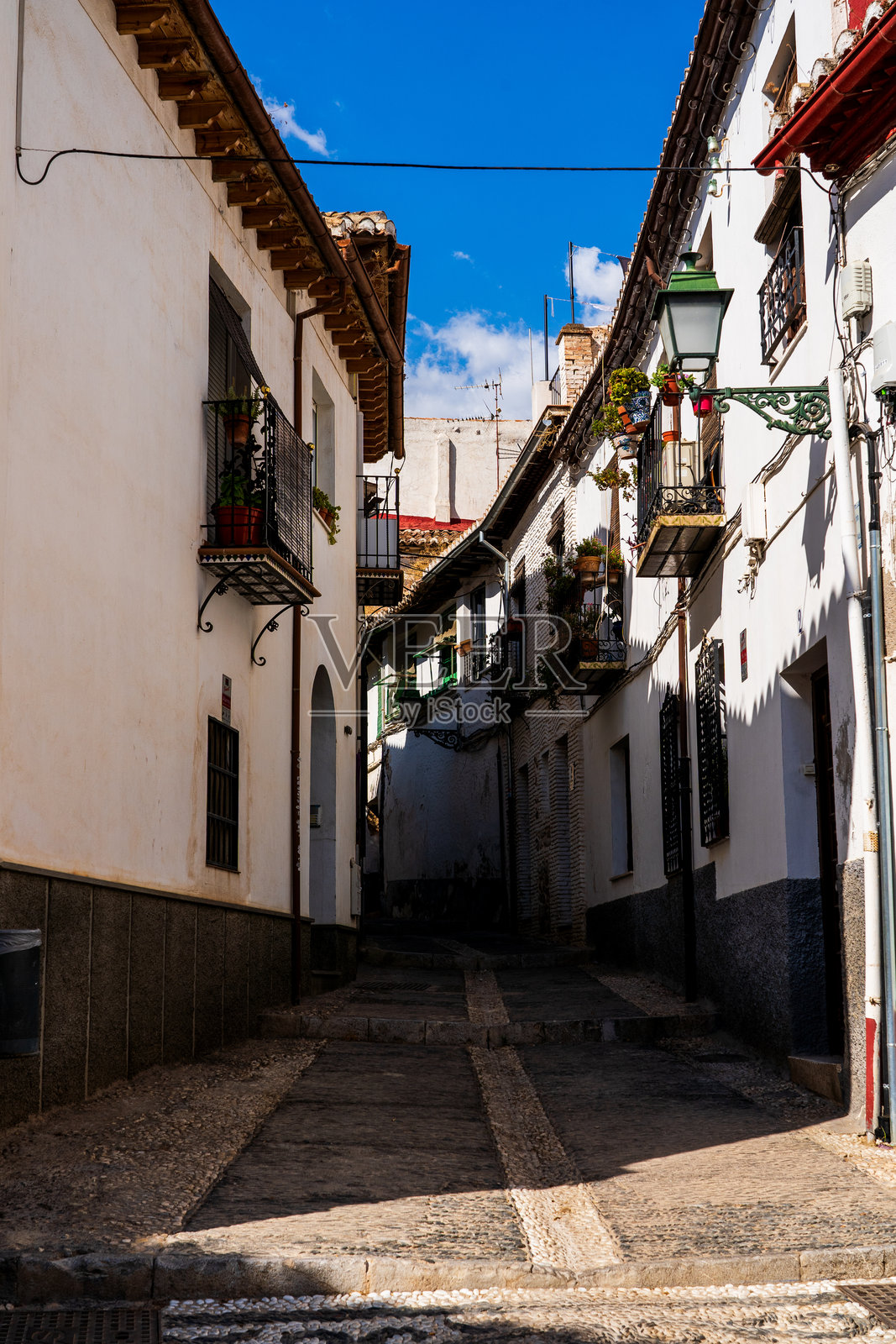 格拉纳达阿尔拜辛区狭窄的摩尔小巷：白色粉刷的墙壁、阳光明媚的阳台，以及充满活力的安达卢西亚温暖光辉中的百年西班牙遗产照片摄影图片