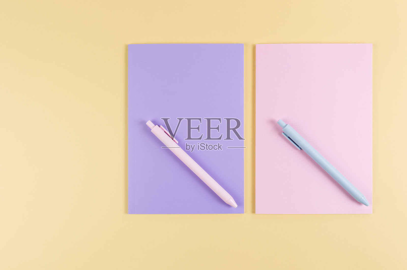 从上方看粉色和紫色的笔记本，粉色和蓝色的笔在黄色背景上。学校，办公室壁纸。照片摄影图片