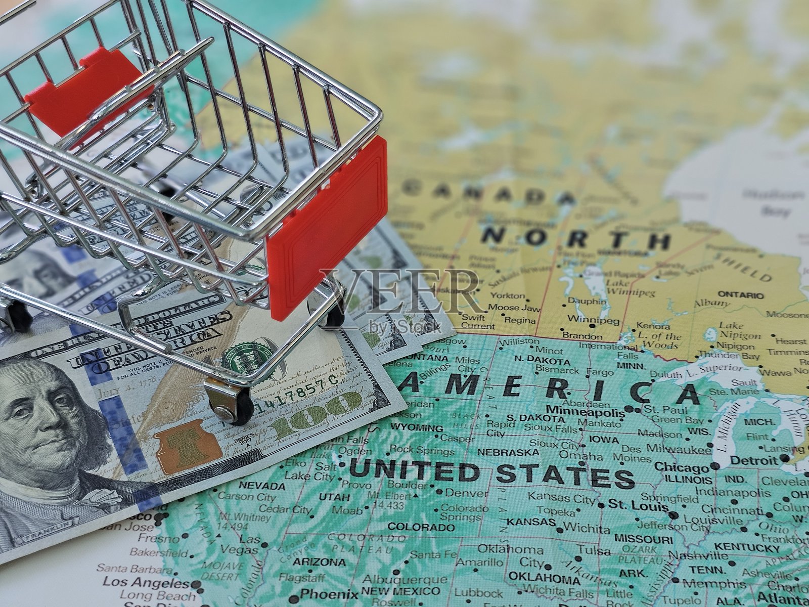 购物车上放着现金，地图上突出显示美国和加拿大，展示了金钱与旅行之间的联系。照片摄影图片
