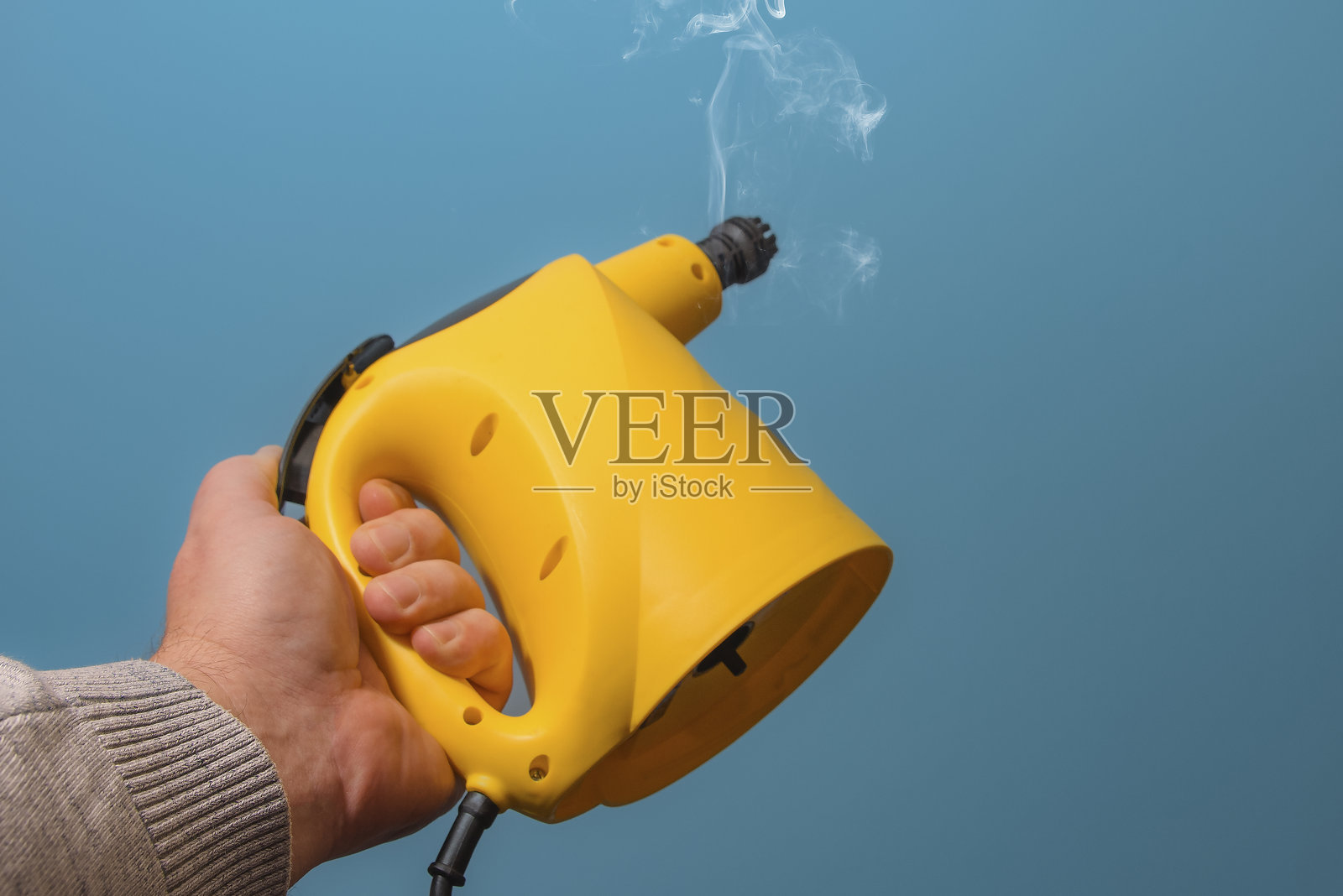 手持黄色蒸汽清洁器，蒸汽从设备中喷出照片摄影图片
