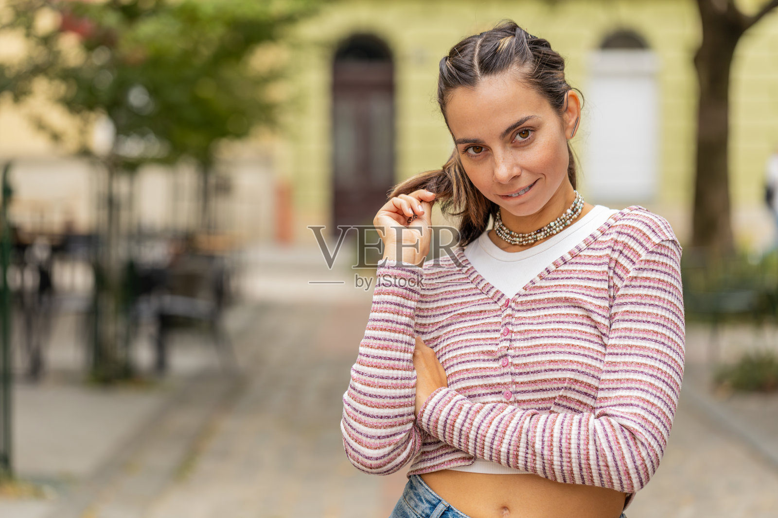 在城市街道上，快乐迷人的年轻女孩害羞地看着镜头并微笑，带着调皮的 flirt。照片摄影图片