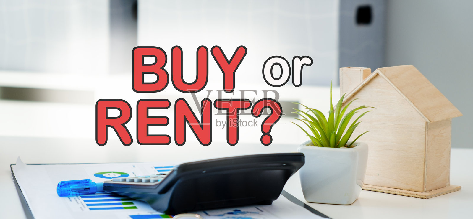 一台计算器放在桌子上，旁边有一栋房子和一盆植物。图像标题为“买还是租”。照片摄影图片