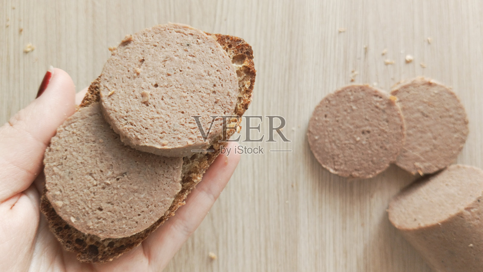 他手里拿着一份肝肠三明治，背景中有一根香肠棒。由内脏制成的肉酱香肠。照片摄影图片