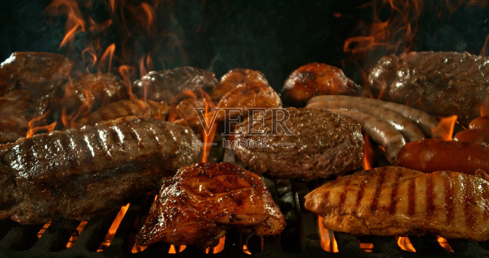 不同种类的炭火烤肉，伴随火焰，背景为黑色。照片摄影图片