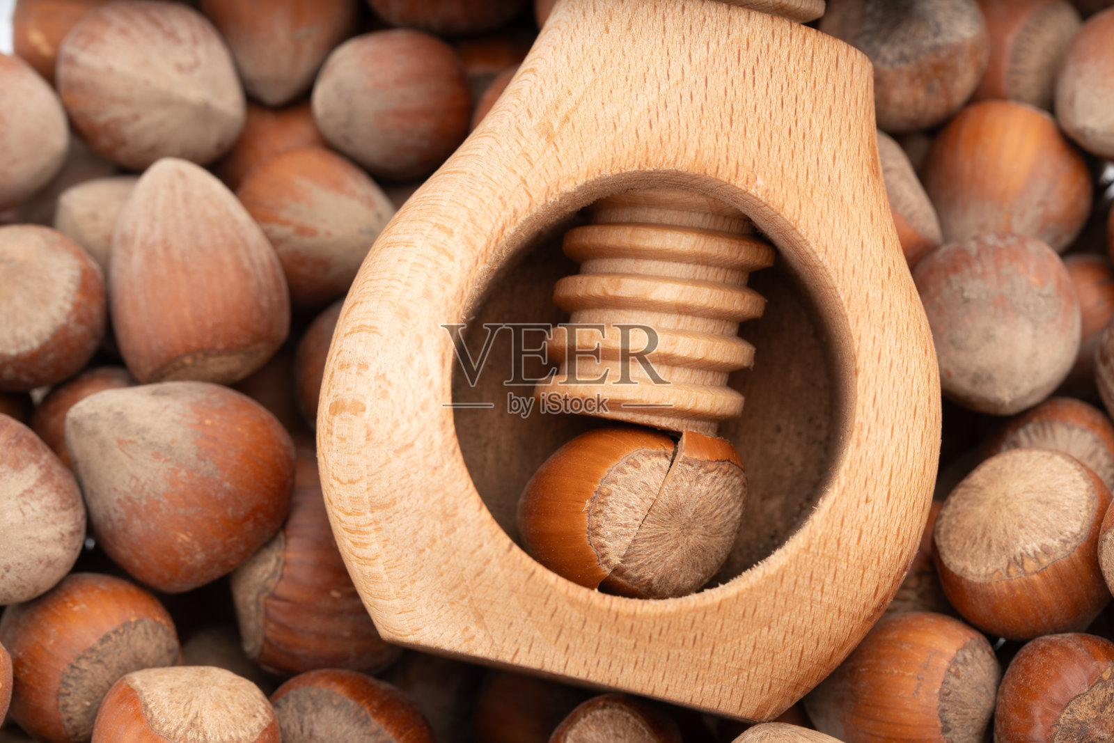特写镜头展示一个木制螺丝坚果夹正在夹破榛子，周围散落着完整的榛子。乡村厨房工具与天然食品的概念。照片摄影图片