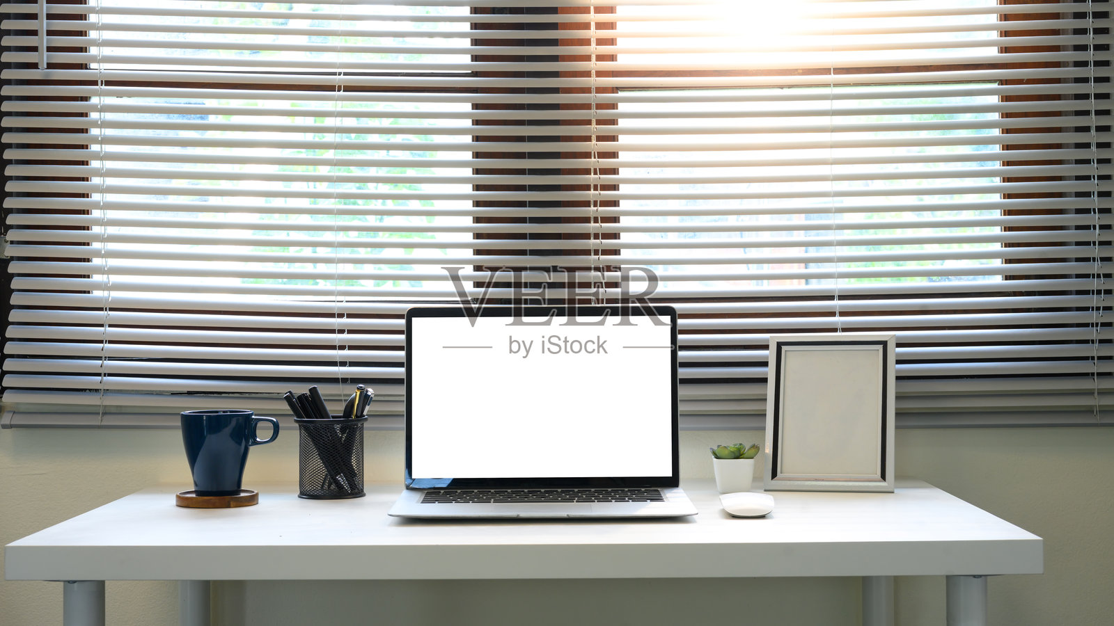 现代家用办公室桌子，前面有一台空白的笔记本电脑屏幕，窗户百叶窗旁边。照片摄影图片