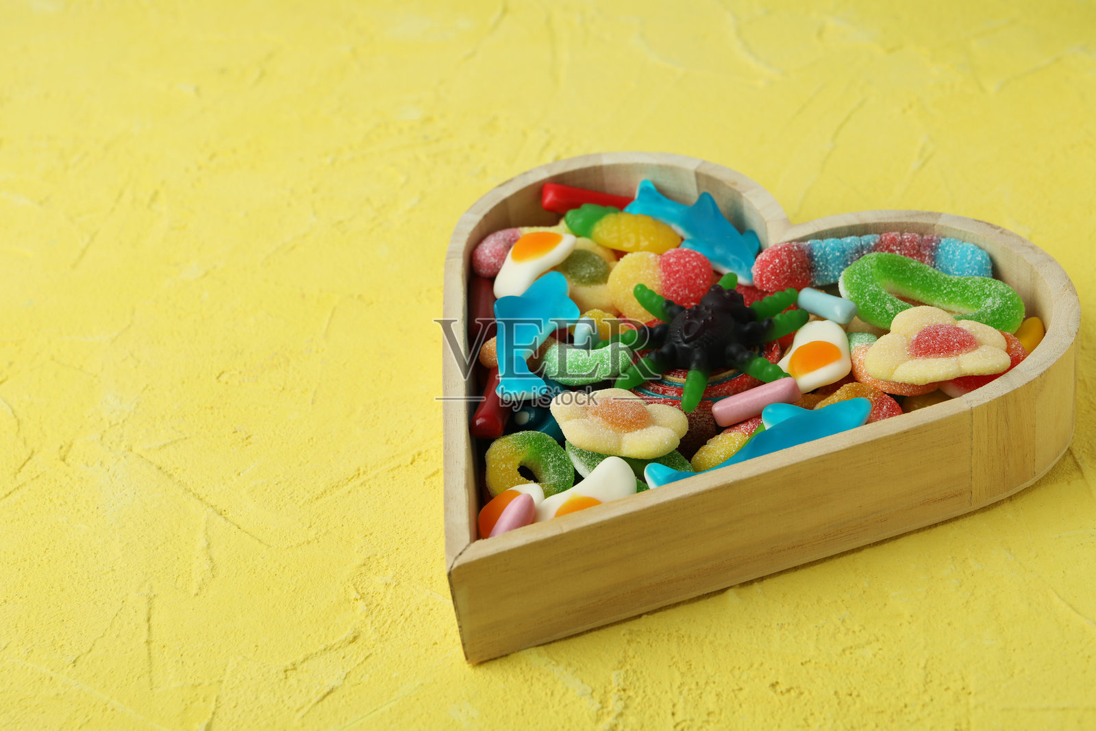 木制心形与橡皮糖在黄色纹理背景上照片摄影图片