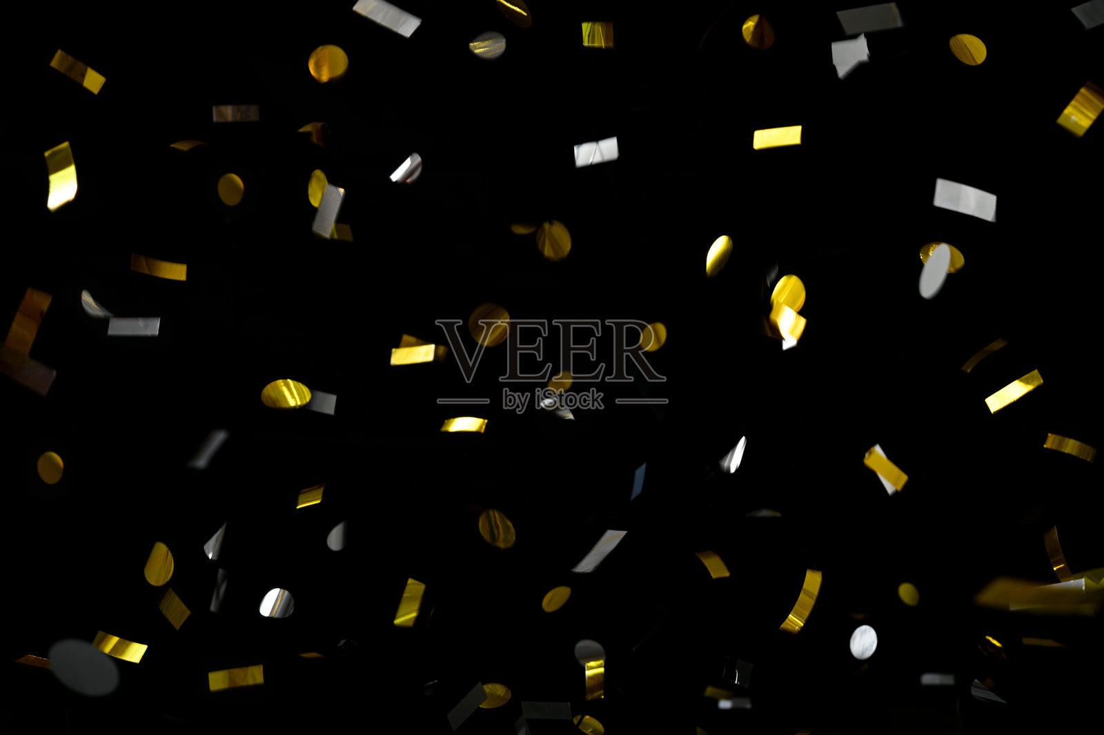 在黑色背景上飘落的闪亮金银色纸屑。照片摄影图片