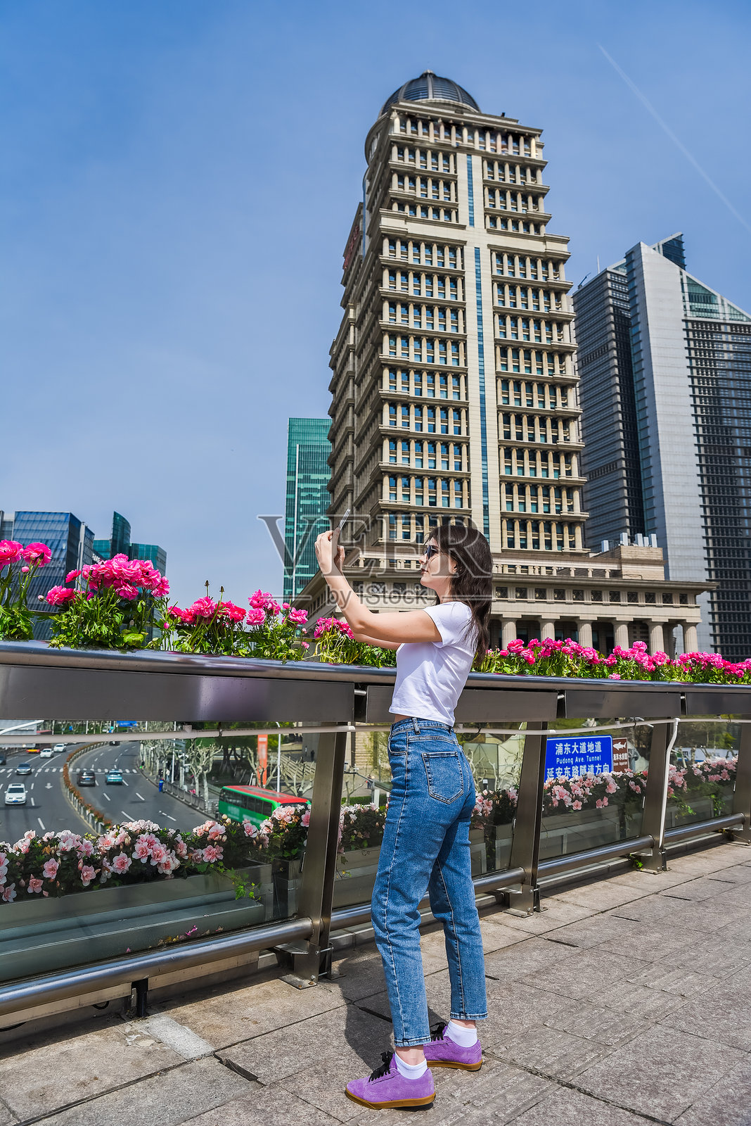 年轻女性在上海浦东的一座人行天桥上拍照，周围是鲜花和现代摩天大楼，阳光明媚的春日。照片摄影图片