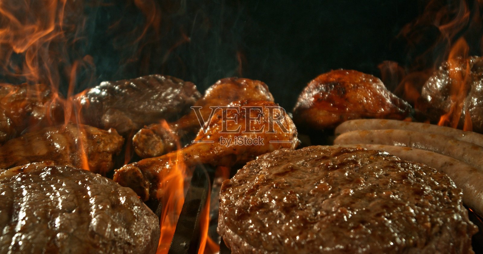 不同种类的炭火烤肉，伴随火焰。背景为黑色。照片摄影图片