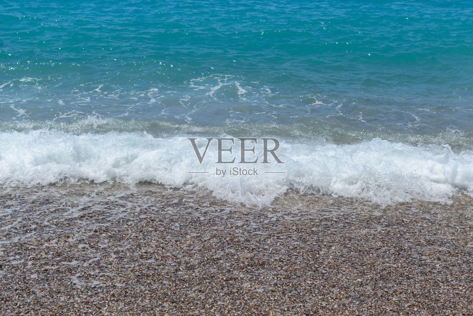 宁静的海滨场景，温柔的碧绿色海浪拍打着卵石海滩。代表着宁静、夏天、假期、大自然的美丽和海岸的宁静。照片摄影图片