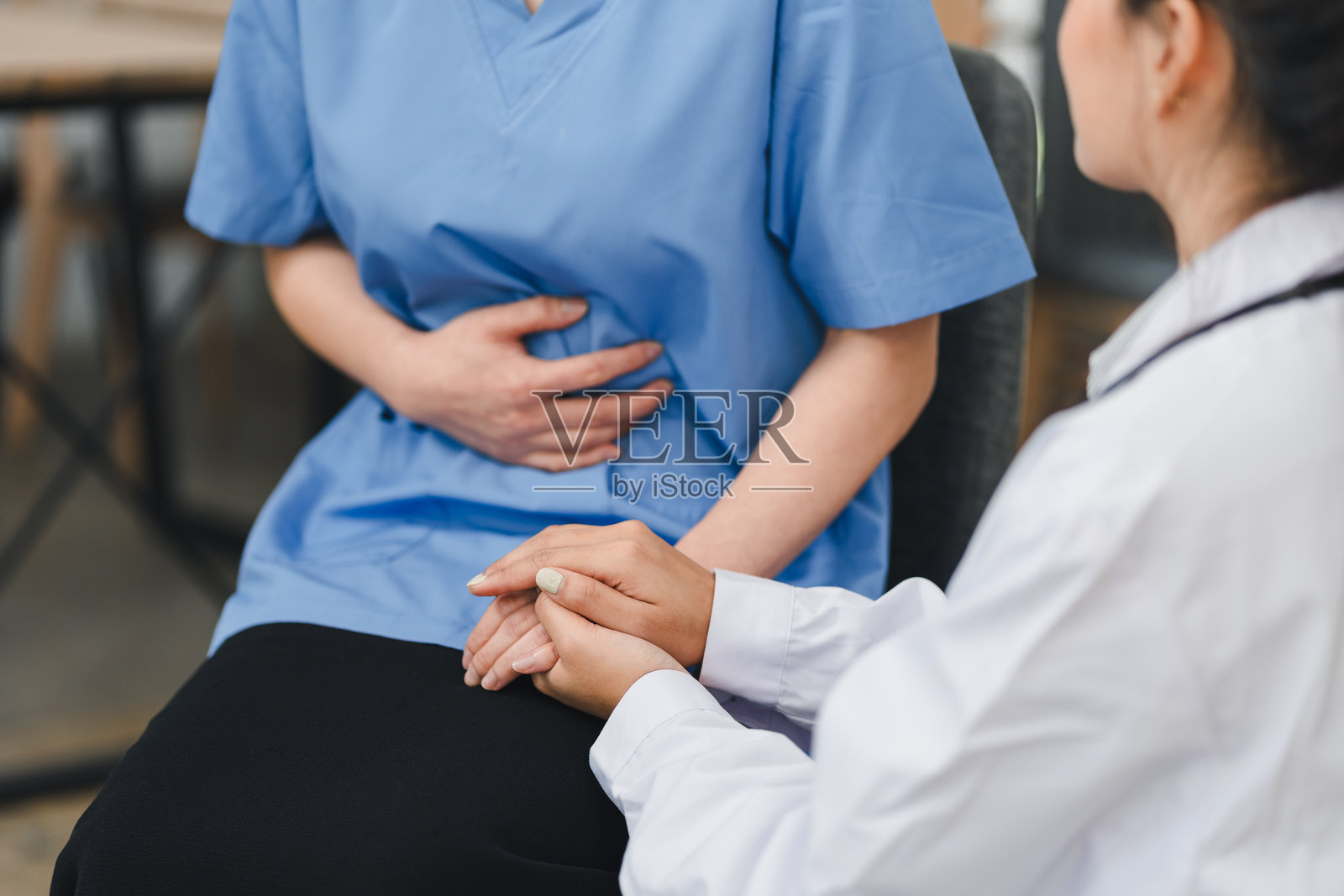 穿着白大褂的医疗专业人员在医疗环境中为穿着蓝色手术服的患者提供安慰，展现出同情和关怀，患者正在经历腹痛。照片摄影图片