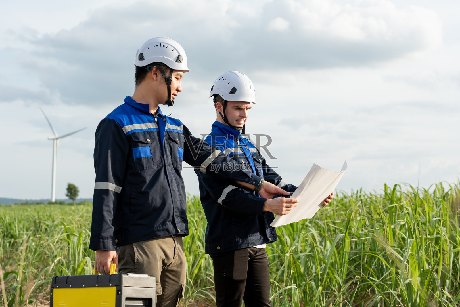 不同民族的男性技术人员在风力涡轮机领域工作。创新工程师们穿着安全装备，在风电场户外致力于开发环保可再生清洁能源。照片摄影图片