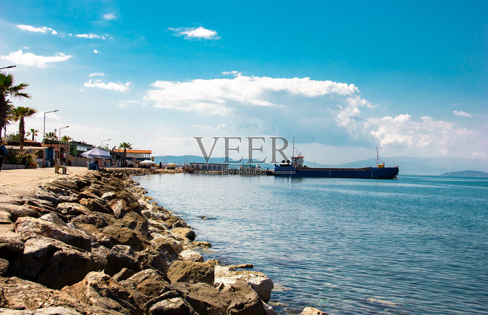 在稍微多云且平静的日子里，远距离拍摄空货船停靠在小船码头。土耳其伊兹密尔的古泽尔巴赫切，2025年4月27日。照片摄影图片