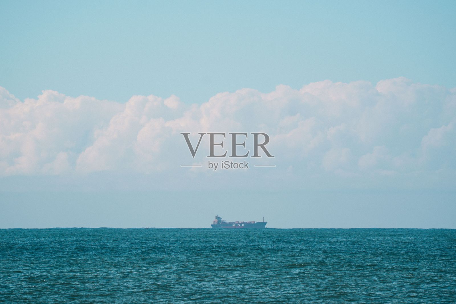 在蓝天下，平静海洋上的货船。照片摄影图片