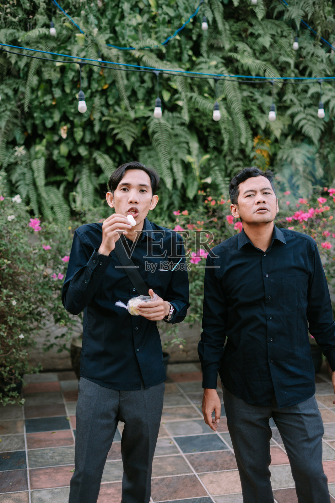 两名男子在郁郁葱葱的花园中，一人沉思地吃着零食照片摄影图片
