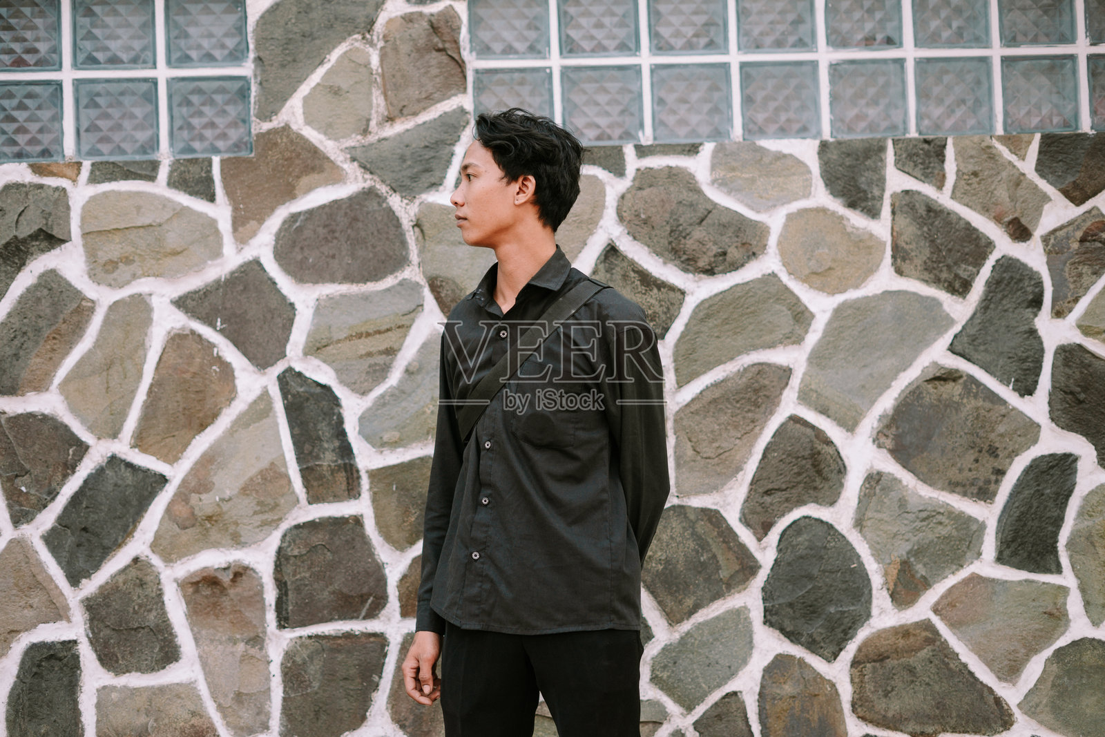 穿着休闲服的年轻男子在石墙前沉思照片摄影图片