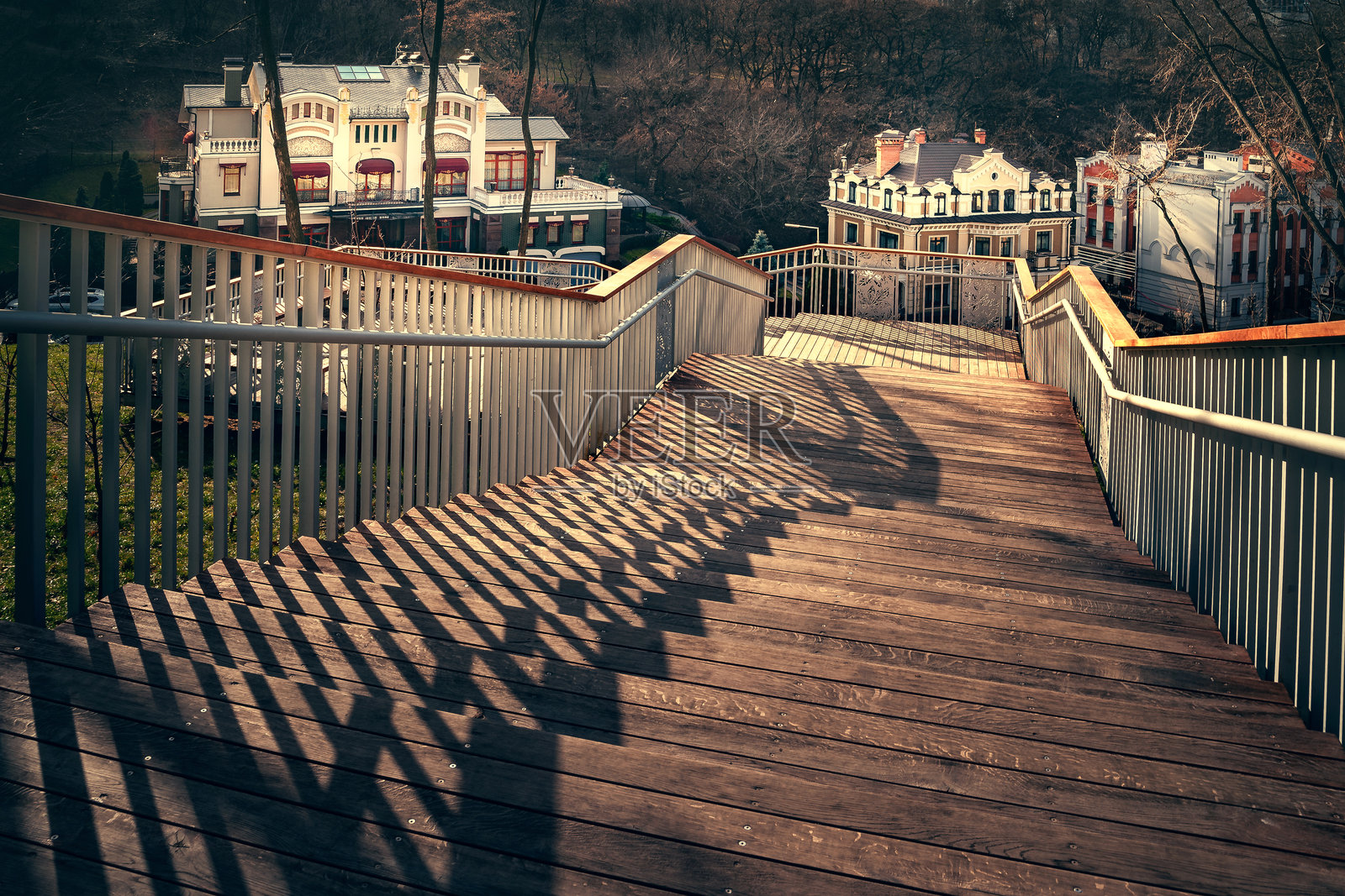 带有栏杆阴影的楼梯。一个从山上下降的楼梯，木制台阶和金属栏杆。傍晚时分的光影交错。照片摄影图片