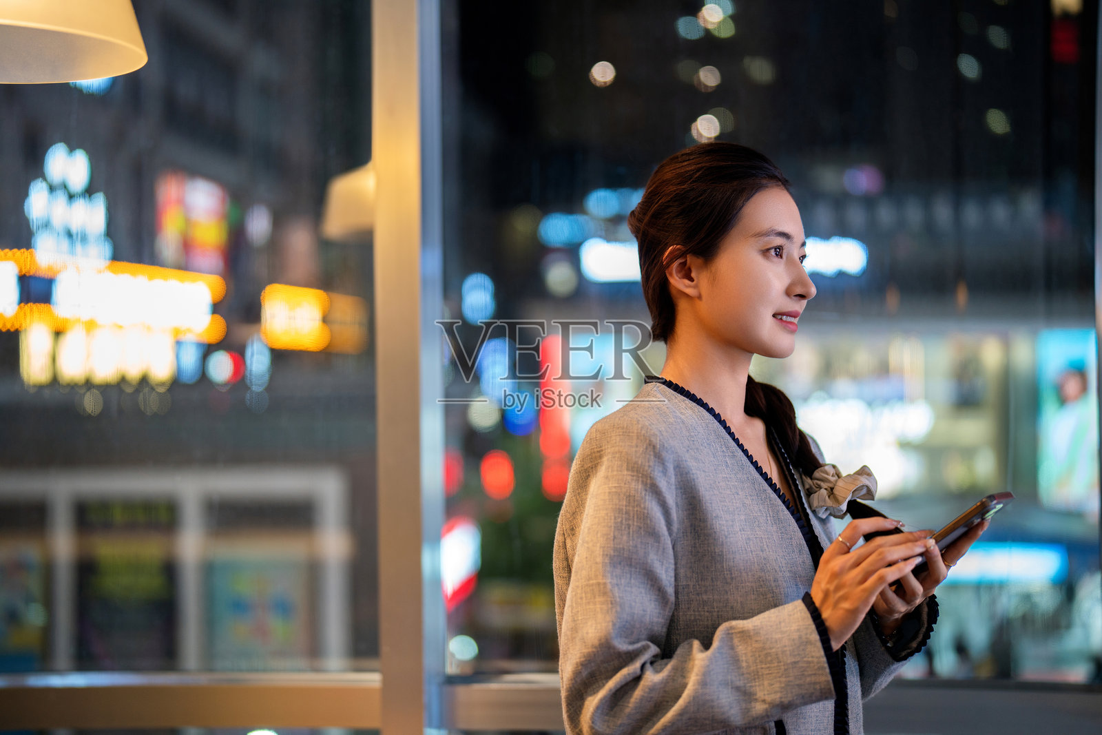 亚洲年轻女性在办公室的窗边夜间使用智能手机照片摄影图片