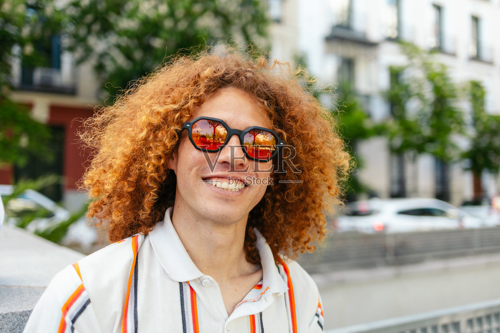 年轻男子在城市环境中微笑，戴着红色头发和太阳镜照片摄影图片