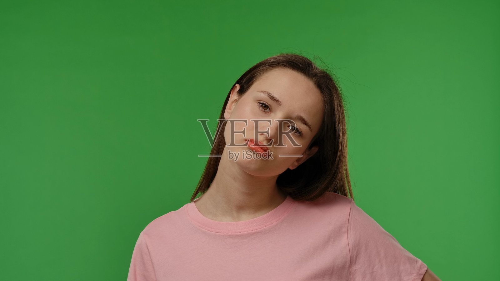 青春女孩在相机前摆姿势，面露愤怒、沮丧和不满的表情，背景为绿色幕布的模拟场景。照片摄影图片