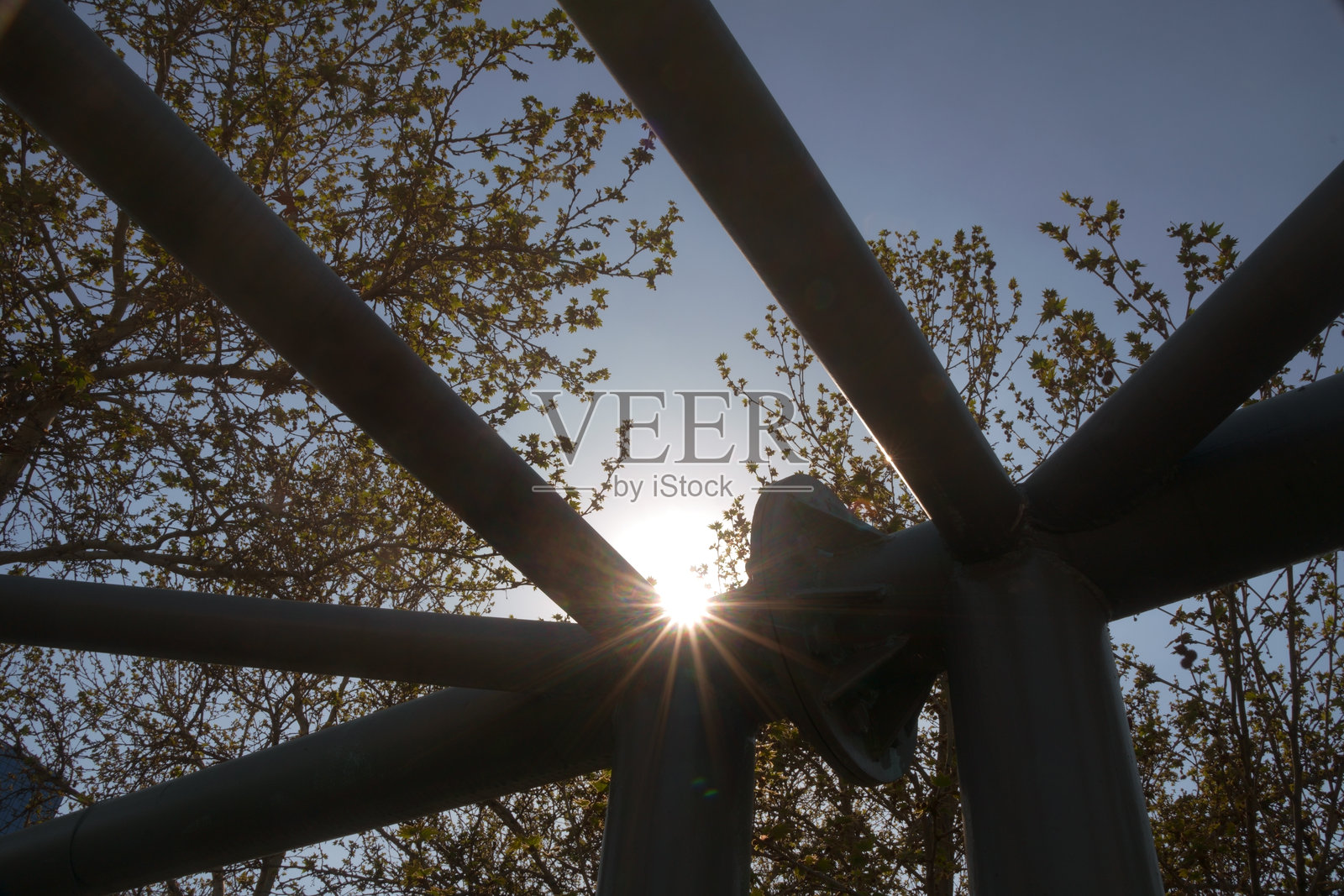 复杂的三角金属桁架框架，背景是树木和蓝天上的阳光照片摄影图片