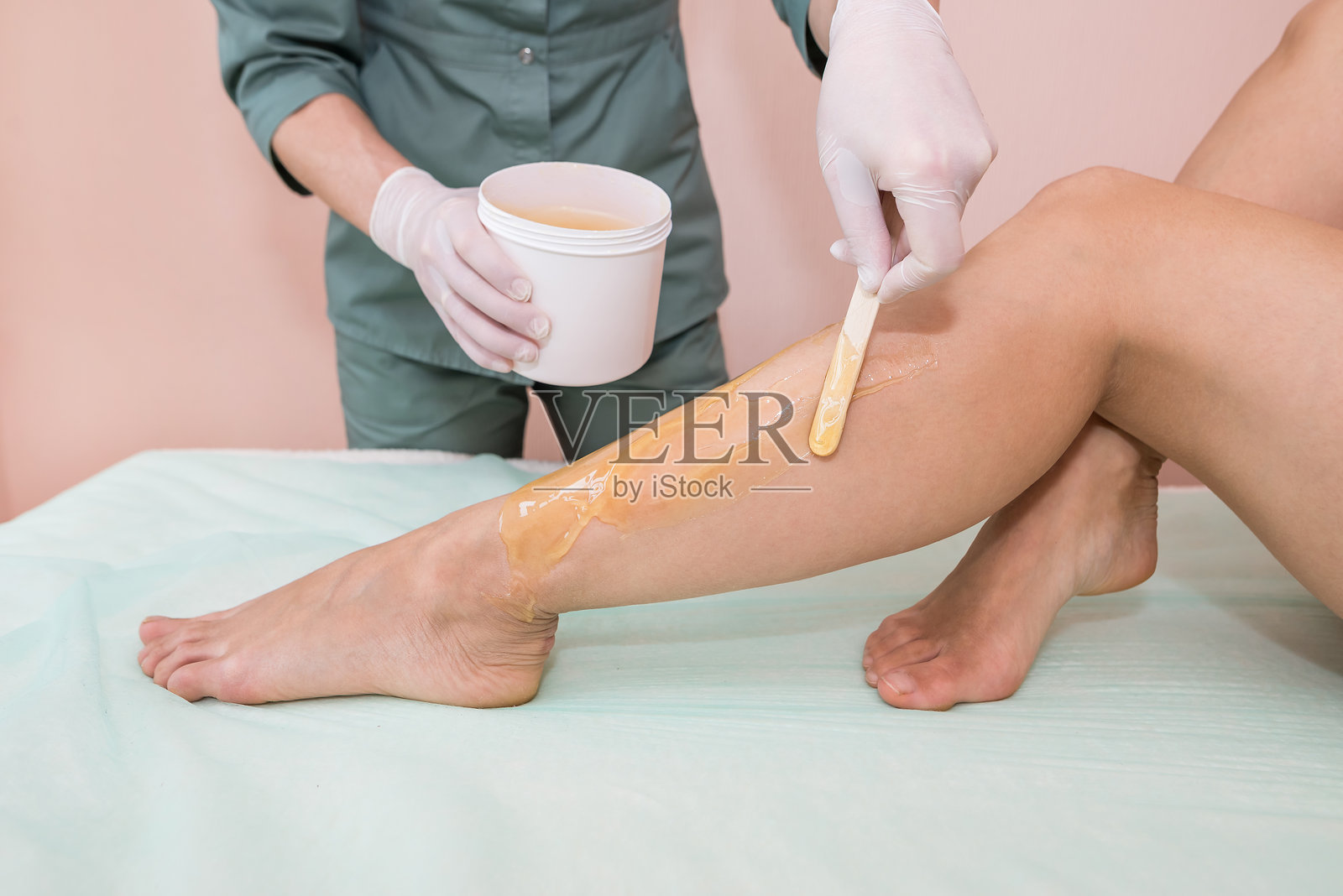 美容师在美容院为女性腿部进行糖膏脱毛。女性美容护理。照片摄影图片